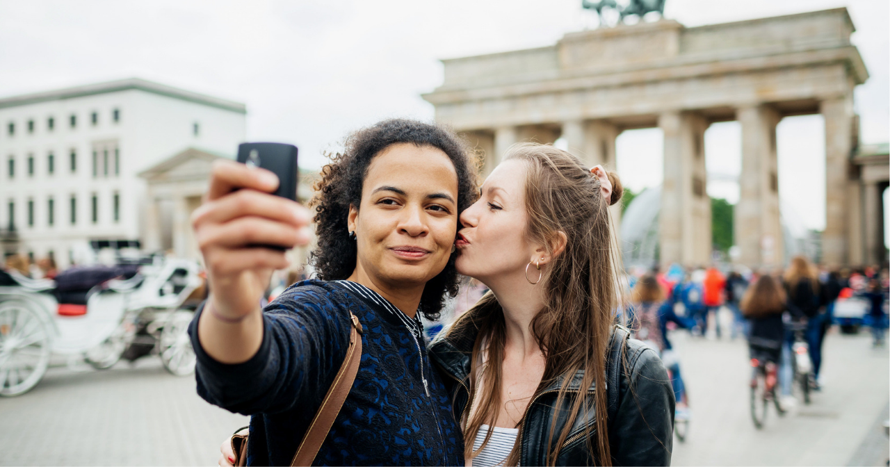 A woman kisses her girlfriend's cheek as they take a selfie