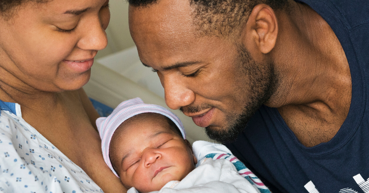 A black mother and father look at their newborn child.