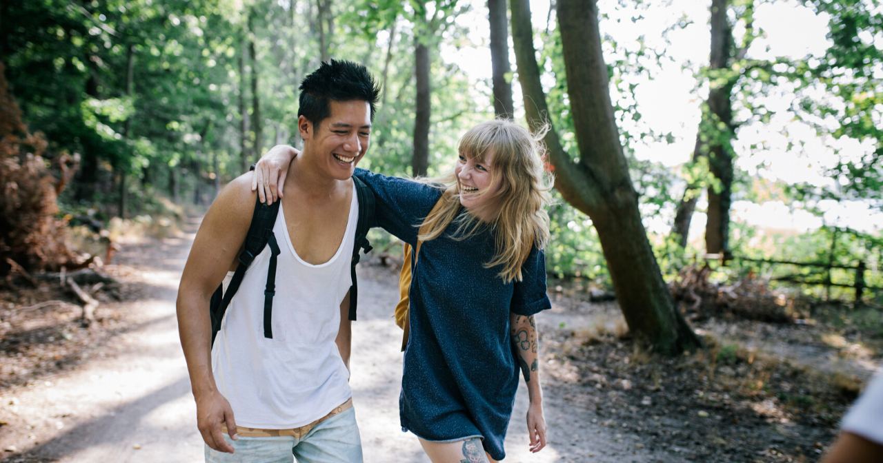 A couple slings their arms over one another's shoulders while hiking. 