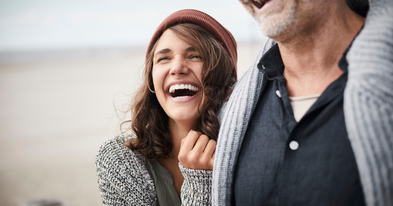 A dad and daughter hug and laugh on a beach. 