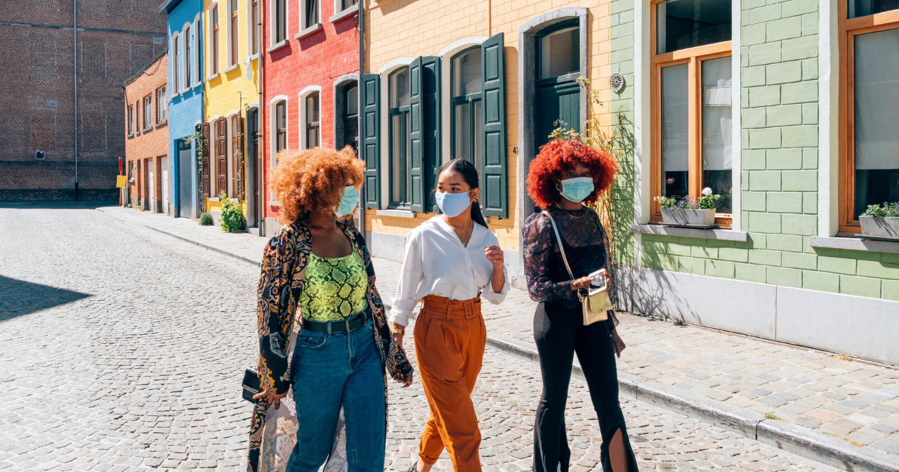 Three friends wearing masks walk down the street and laugh. 
