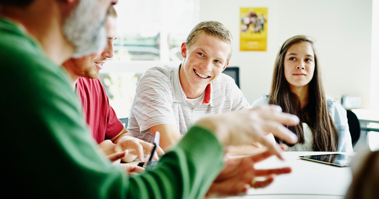 A male teacher laughs with his students as they talk together. 