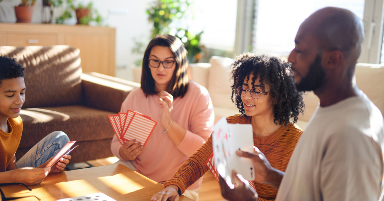 A family of four sits around their coffee table and plays a card game with oversized cards. 
