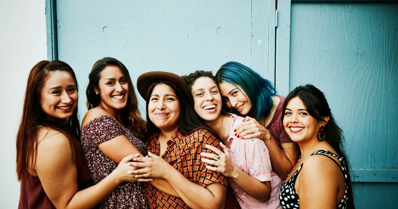 Six smiling Latina women hug. 