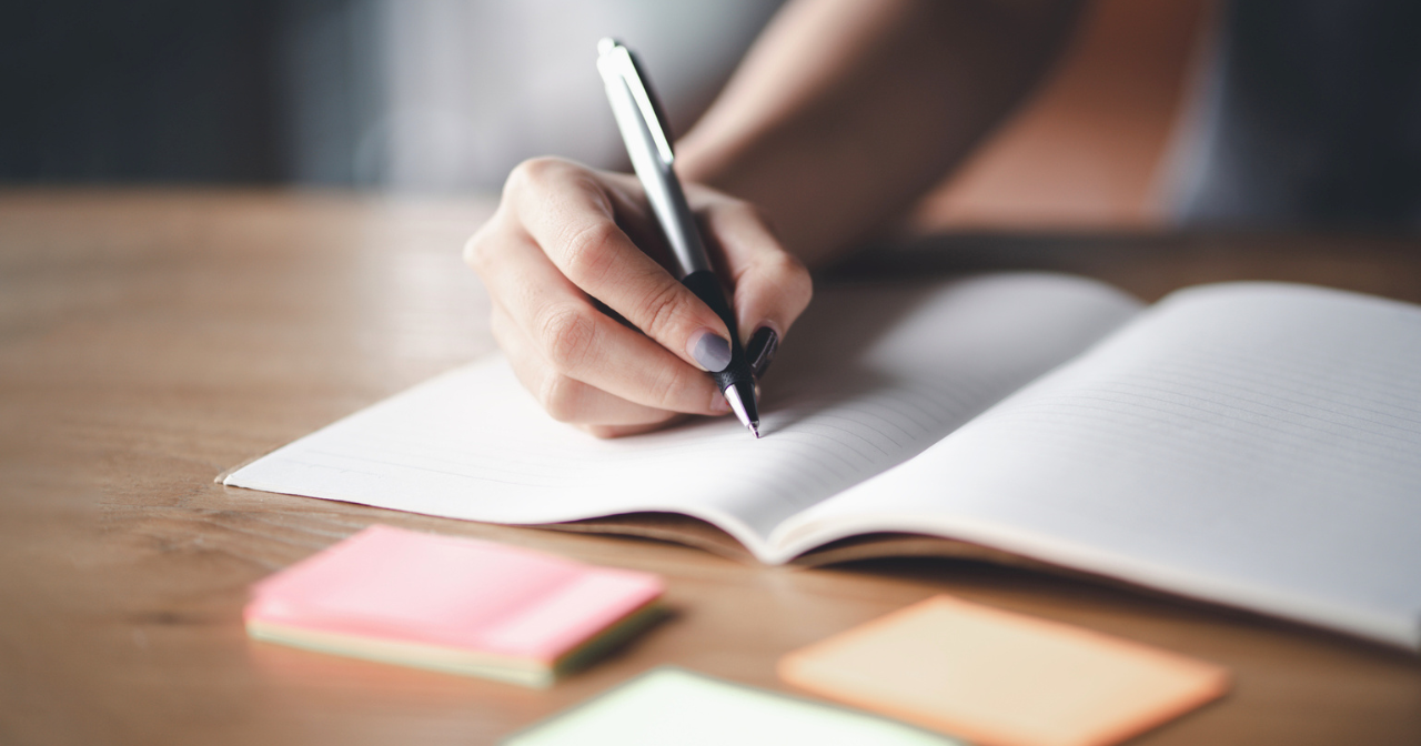 A hand holds a pen over a blank sheet of paper.
