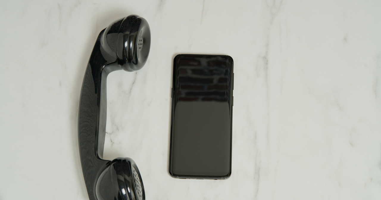 A black landline phone sits next to a black cell phone on a table.