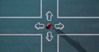 An overhead photo of a woman dressed in red stands in the middle of a painted intersection deciding which way to go. 