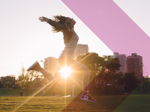 A woman jumps for joy in a field with the sun behind her