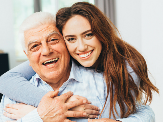 A daughter hugs her father from behind. 