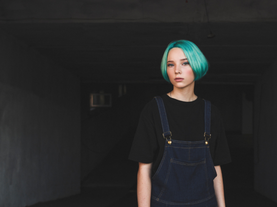 a teen with blue hair stands in an empty room
