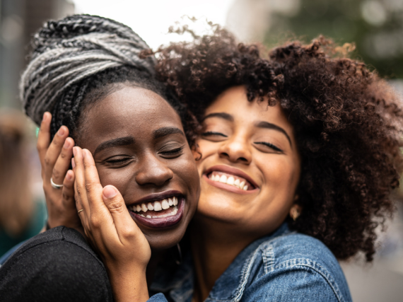 Two women hug very closely with large smiles