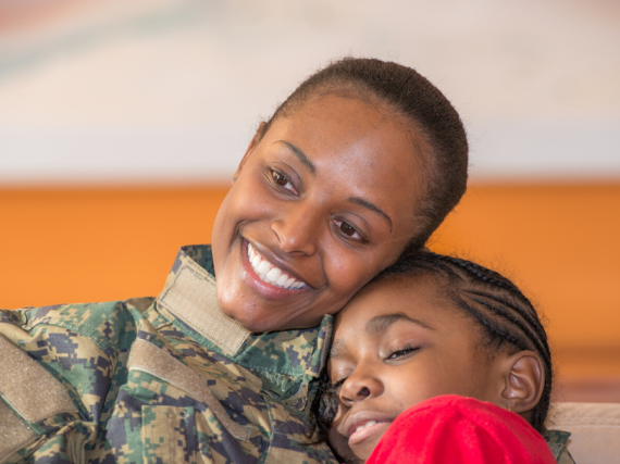 A black woman in a military uniform hugs her daughter. 