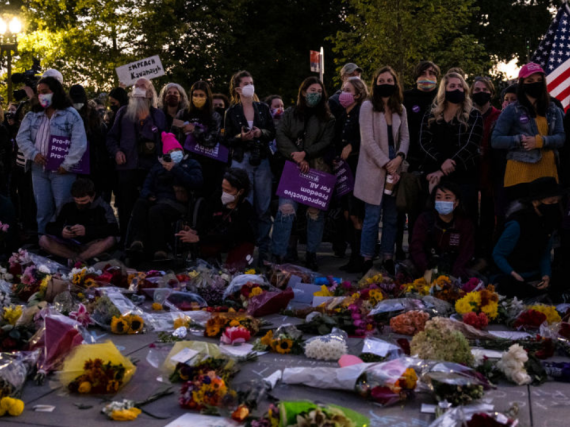 A group of mostly women standing in front of flowers and posters outside the Supreme Court. 