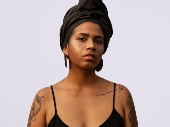 A Black woman looks directly into the camera, seriously. 