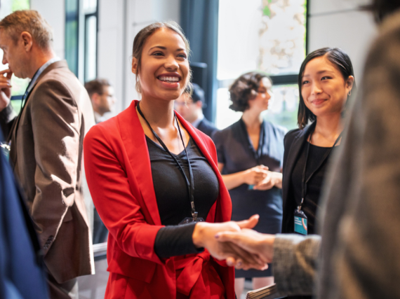A woman in a red jacket shakes hands with someone at an event. 