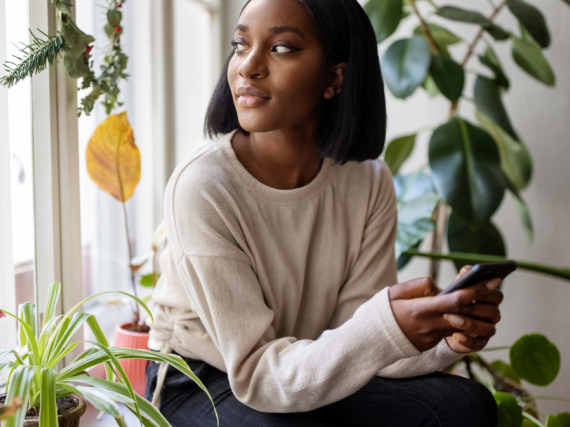A Black woman sits next to a window and looks out contemplatively. 
