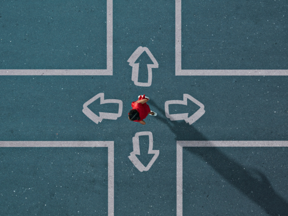 An overhead photo of a woman dressed in red stands in the middle of a painted intersection deciding which way to go. 